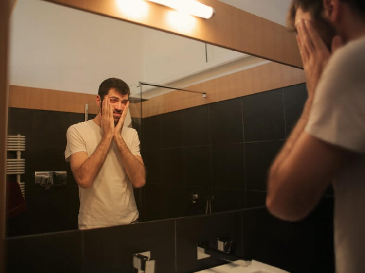 Sad guy holding his face in mirror
